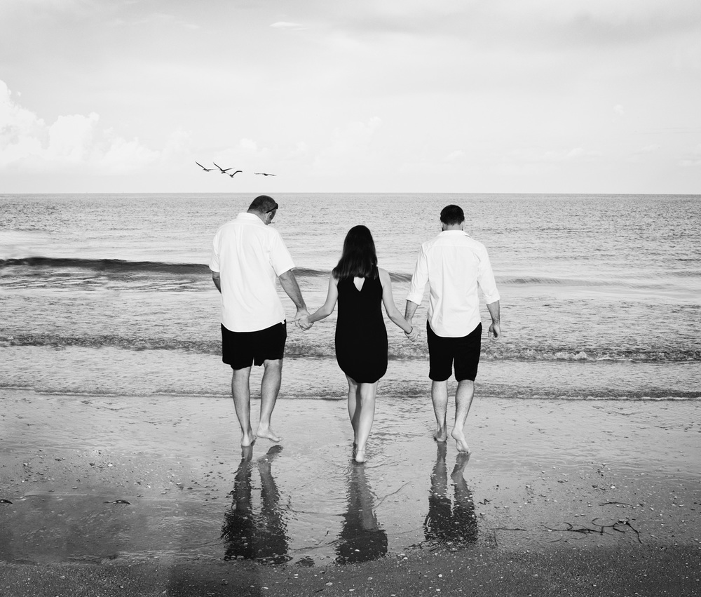 A candid black and white photo of father, daughter and son-in-law walking into the water at Pass-a-Grille Beach.