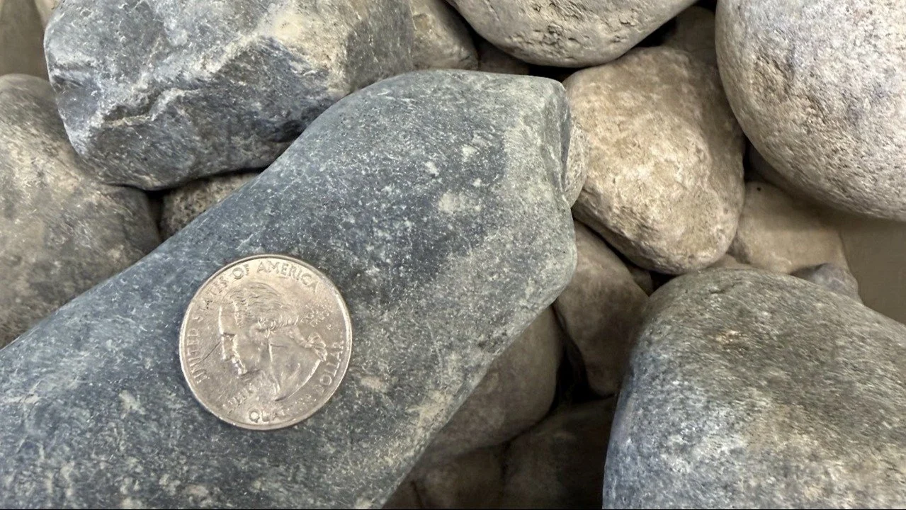 A quarter dollar coin placed on a gray stone among other rounded stones.