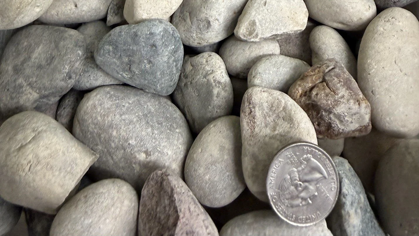 A collection of various smooth, rounded rocks with a quarter coin for size reference.