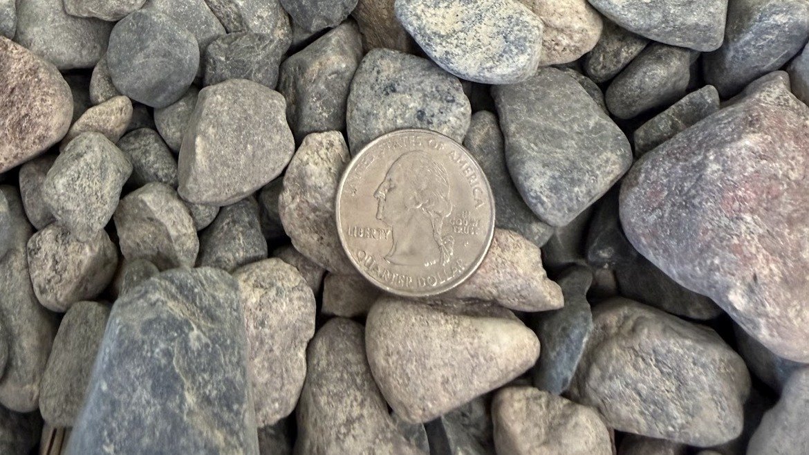 A quarter dollar coin surrounded by various small gray rocks.