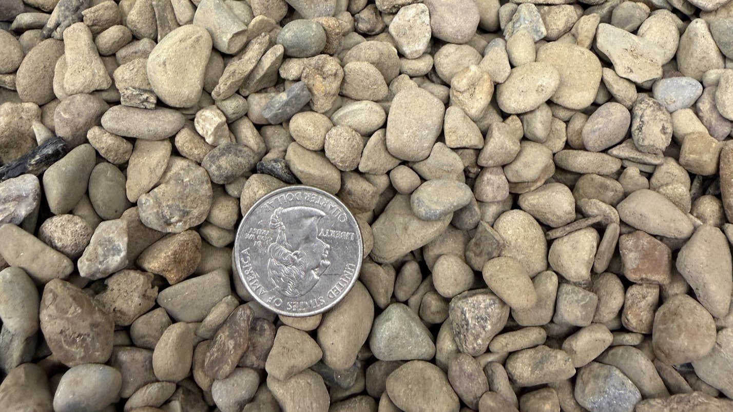 Close-up of a pile of small, rounded rocks with a quarter coin for size reference.