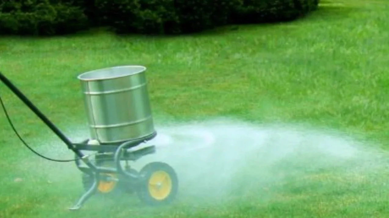Lawn tractor spraying herbicide or fertilizer onto grass in a field.
