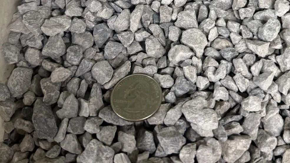 Close-up image of small, irregularly shaped gray rocks with a quarter coin for scale.