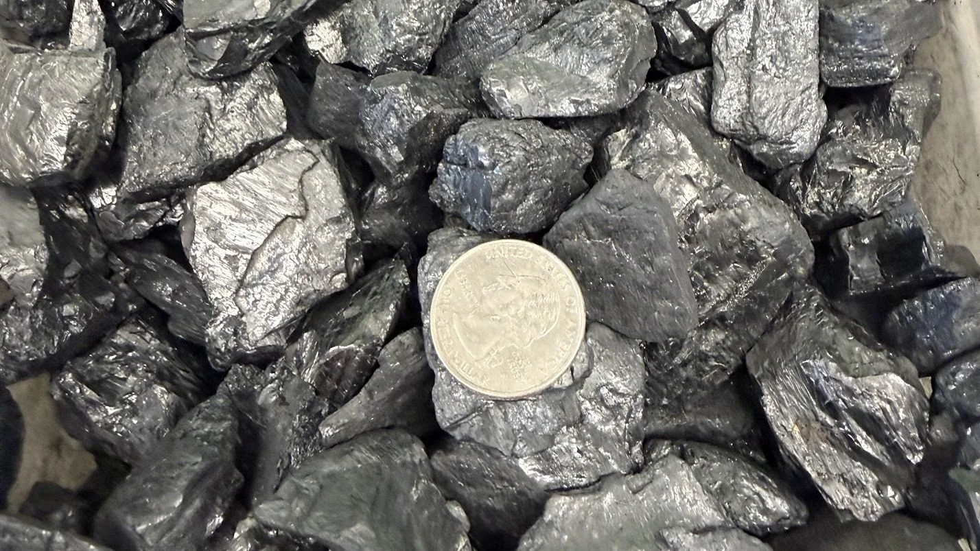 A pile of black, shiny, irregularly shaped rocks with a quarter coin placed on top for scale.