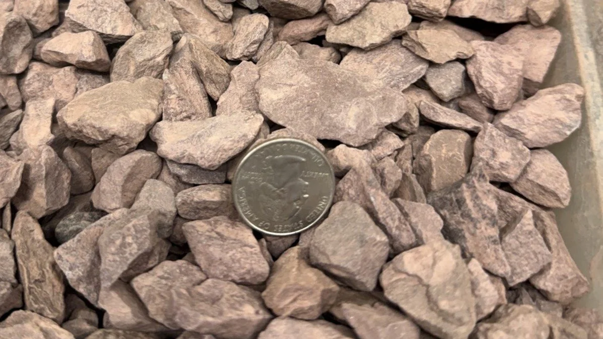 A pile of pinkish-gray rocks with a U.S. quarter for size reference.