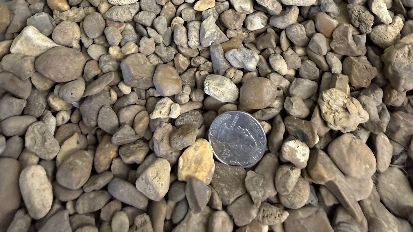 Close-up of a collection of small rocks and gravel with a quarter dollar coin for size comparison.