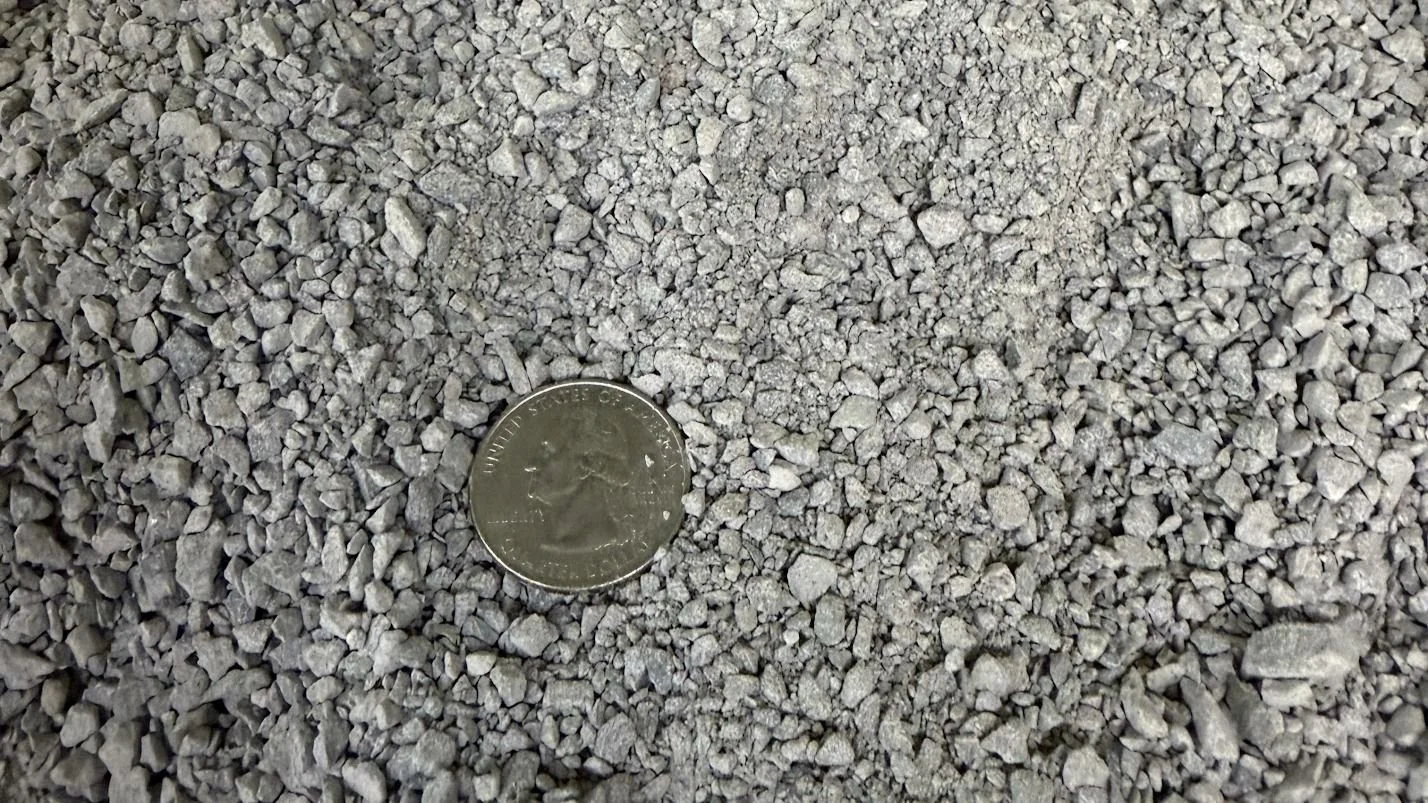 Close-up of gray gravel with a quarter coin for size reference.