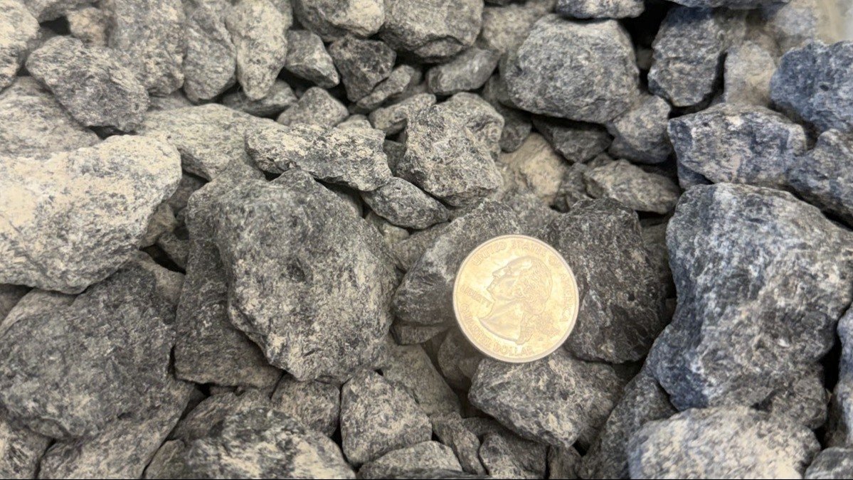 A close-up view of gray, jagged rocks with a U.S. quarter dollar coin for size reference.