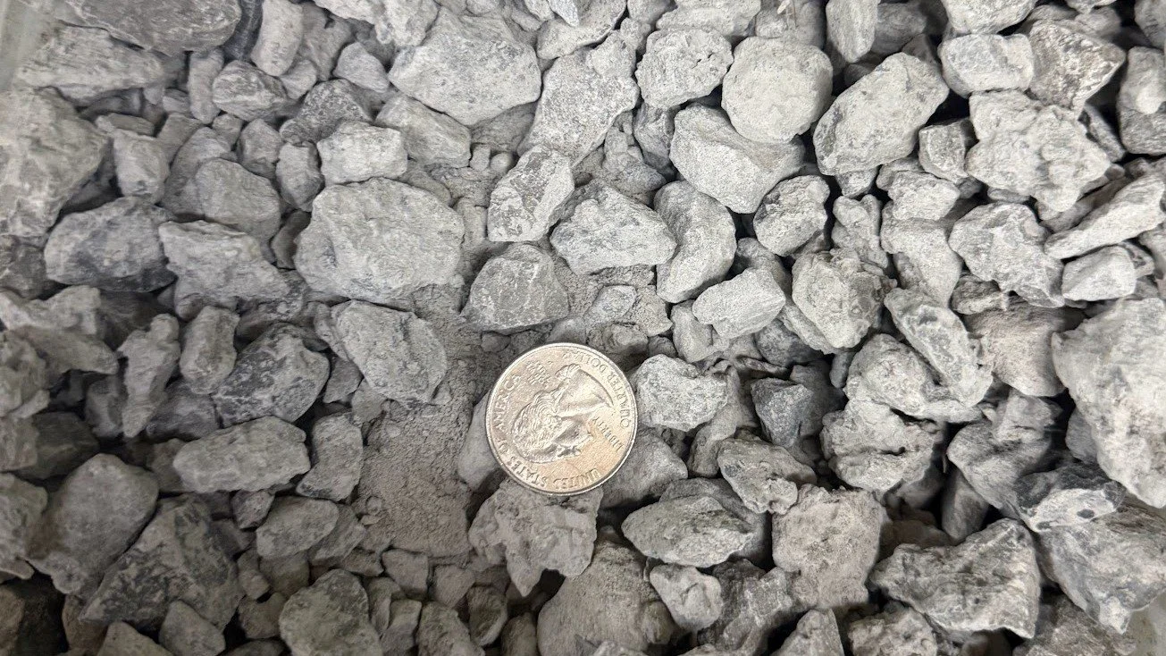 Close-up of gray gravel stones with a quarter coin placed among them for size comparison.