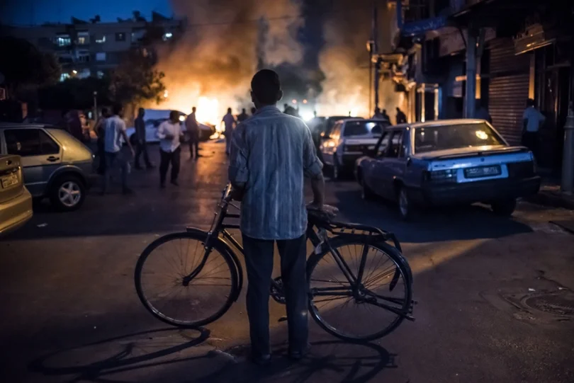 Damascus, Syria, 24 August 2013© Sergey PonomarevA cyclist watches a fire caused by the explosion of a mortar shell during fighting between Government and Opposition forces near the Old City of Damascus.