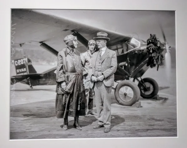 "Mrs. D.W. Barnes of Portland celebrated her 90th birthday on June 27, 1928 by taking her first ride in an airplane. Her son E.L. Barnes (possibly the man on the left) accompanied her in a Ryan monoplane flown by pilot Gordon Mounce (possibly the man in the background). More than two dozen family members and friends turned out to watch. Mrs. Barnes was an avid follower of aviation news, the Journal reported in a brief article, and had been planning the flight for quite a while. At the end of it, she "landed breathless and pleased," the Journal reported."
