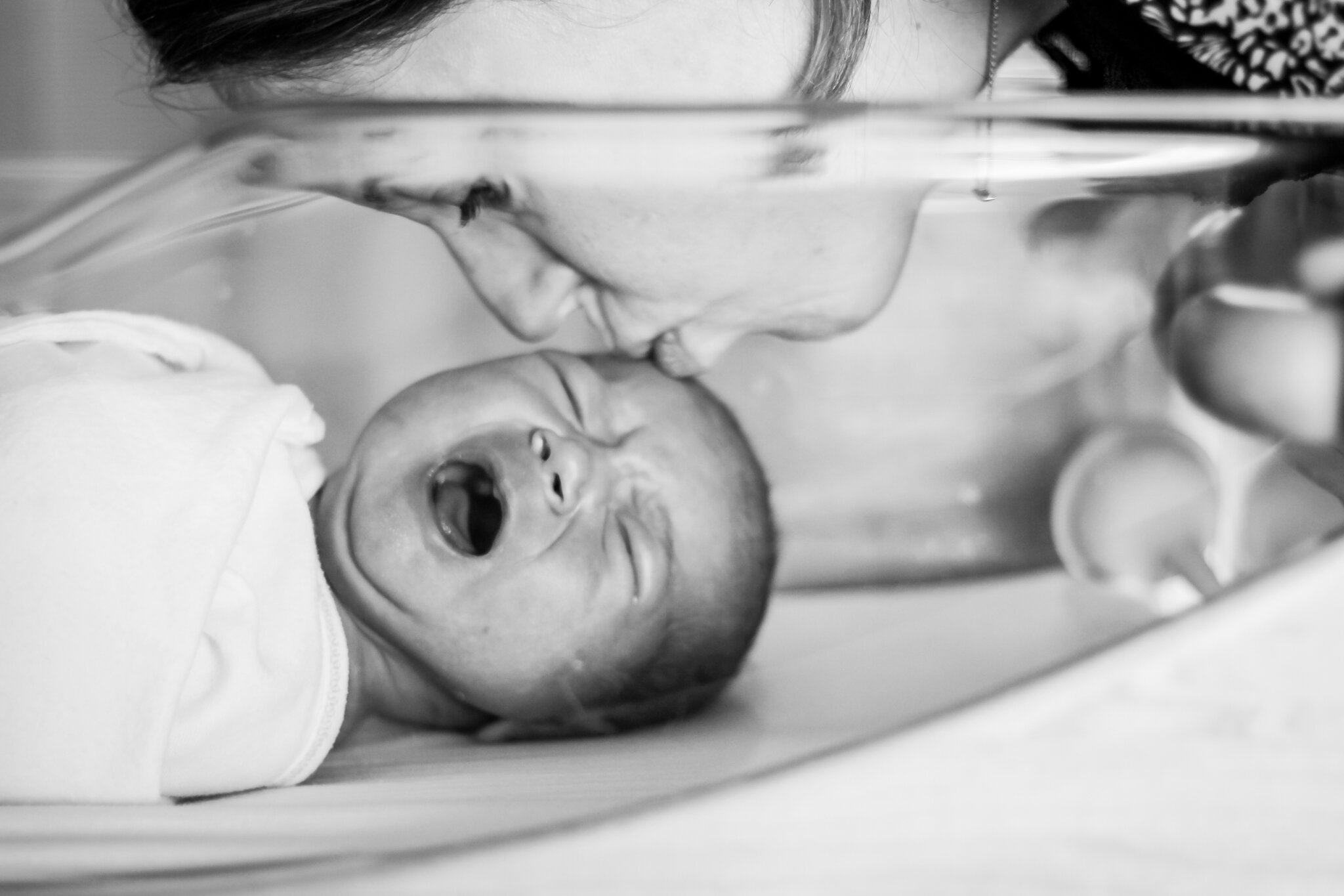 mom kissing newborn in hospital bassinet