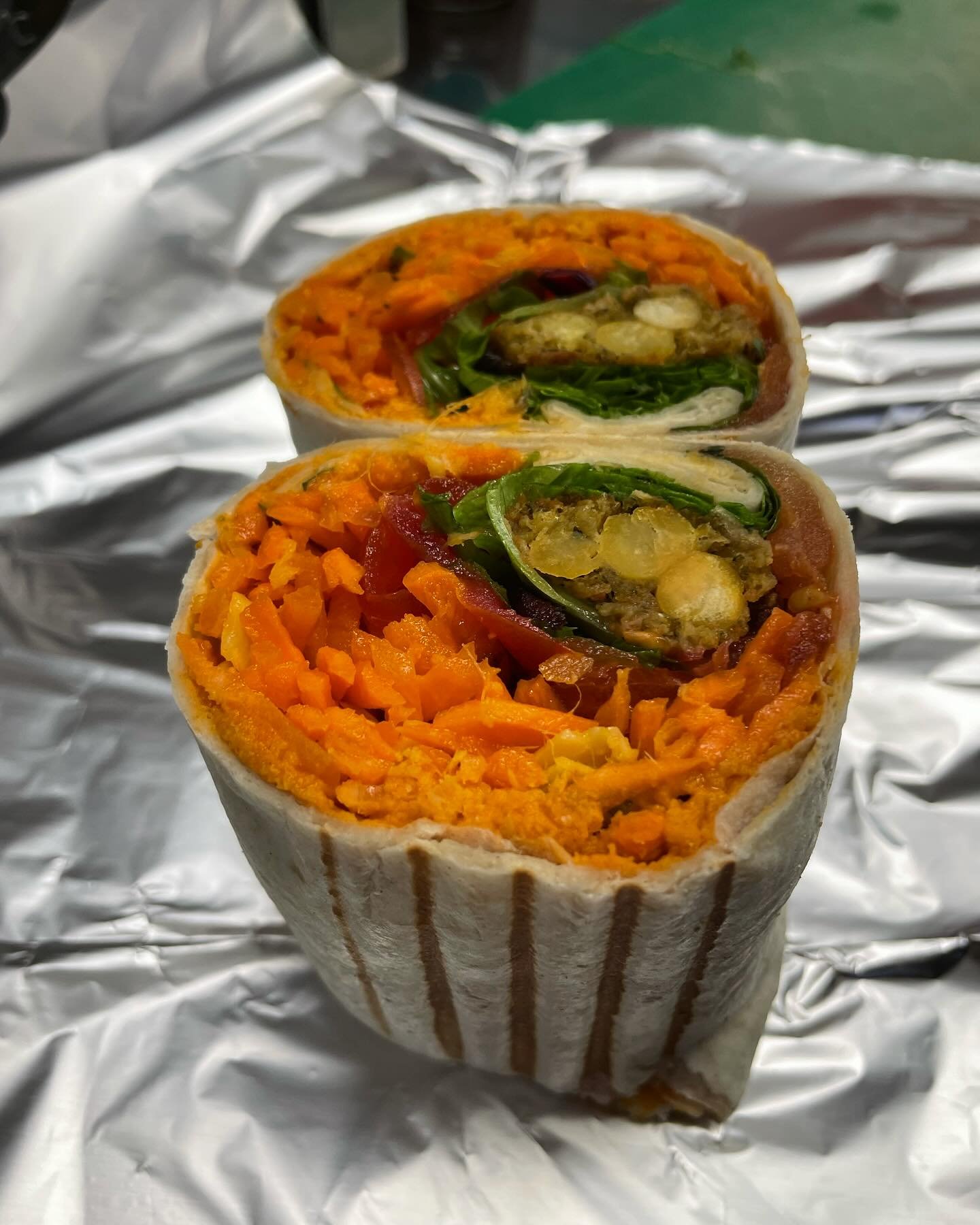 🥙 Our falafel wrap is filled with homemade paprika hummus, carrot slaw 🥕 with ginger 🫚, toasted flaked almonds, fresh coriander and chilli flakes 🌶️, tomatoes 🍅, salad leaves 🥗 and the delicious hot sauce from @firelli which we also sell on the