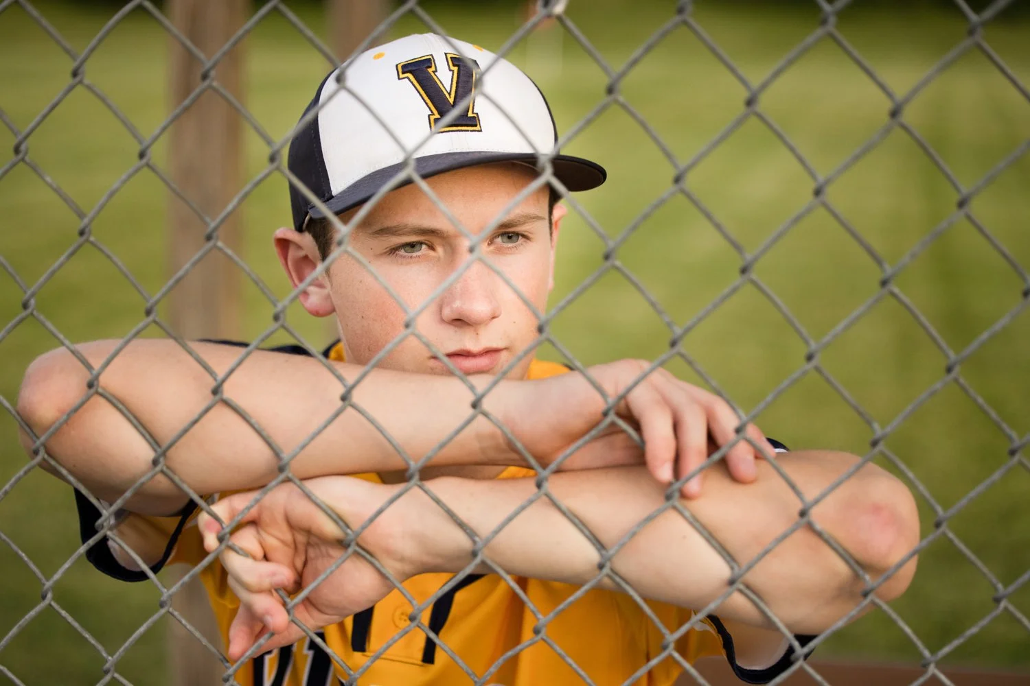 Victor NY senior pictures featuring high school baseball player leaning on fence