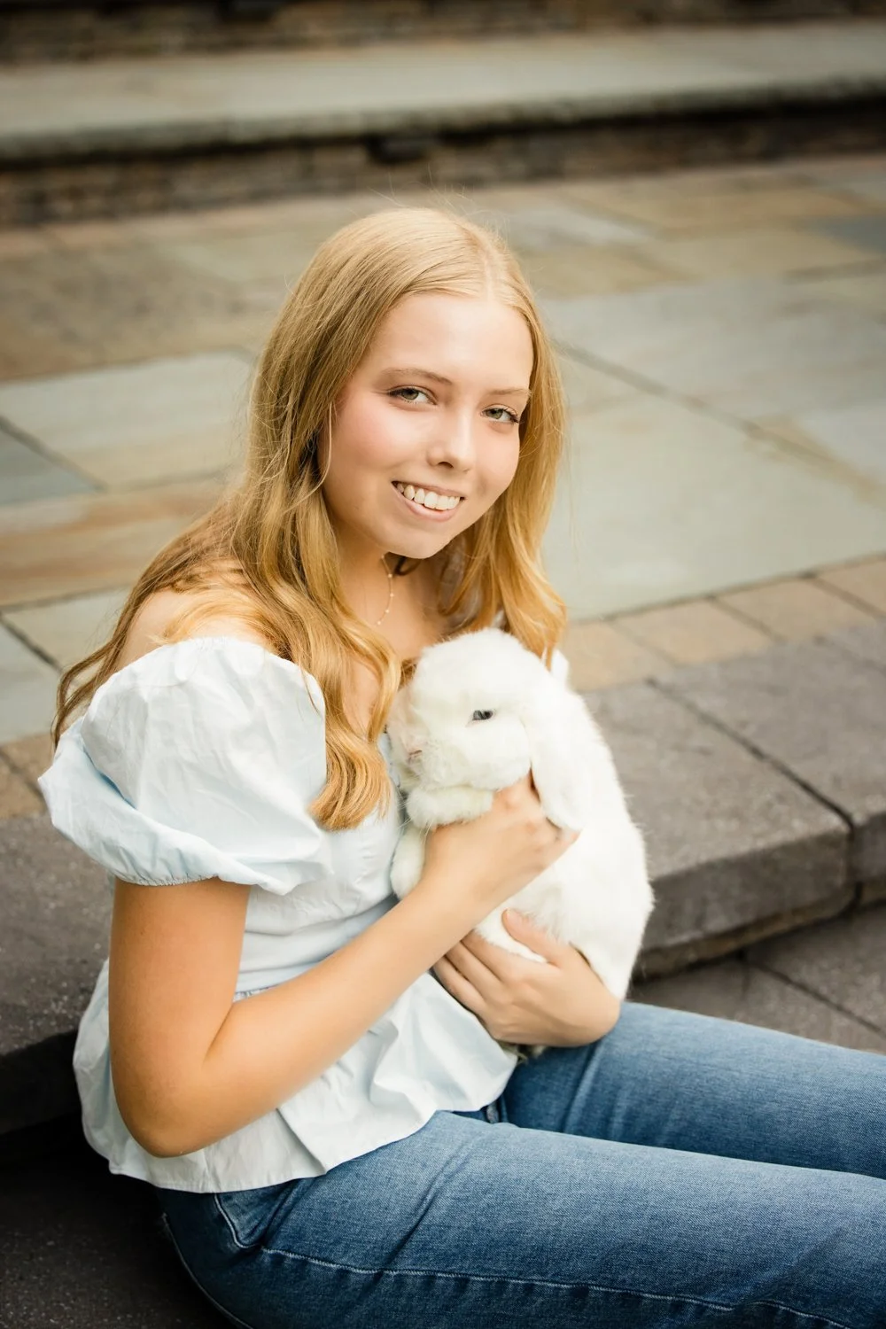 High school senior sitting on sidewalk holding pet rabbit during Rochester NY senior portraits