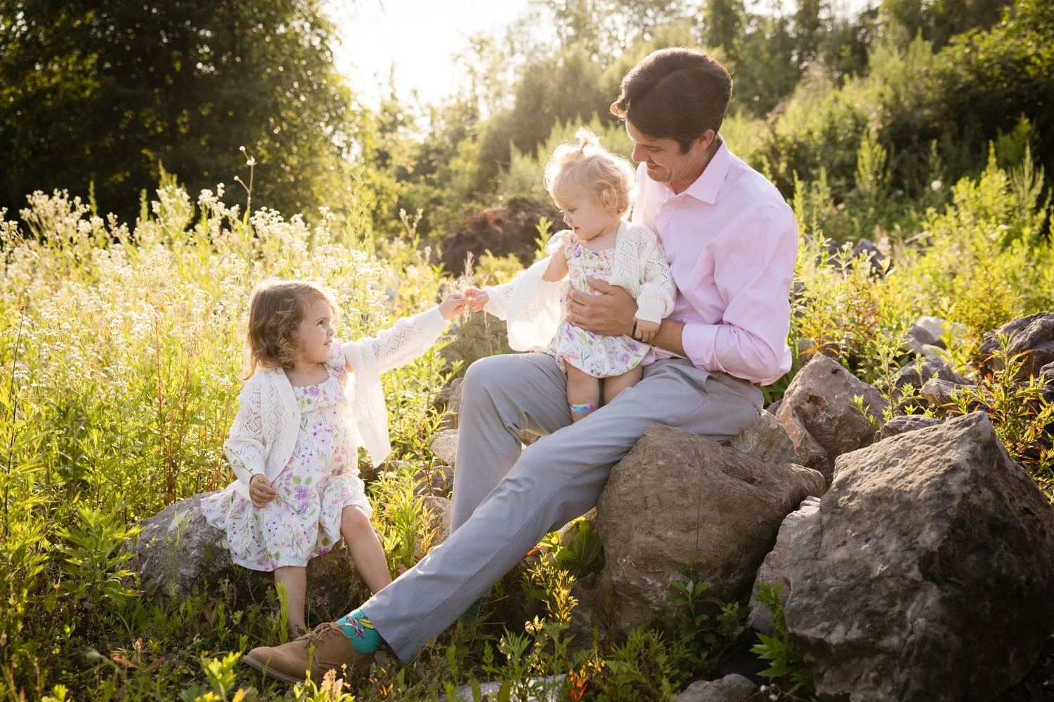 Family photo session in Fairport NY capturing father and daughters in wildflower field