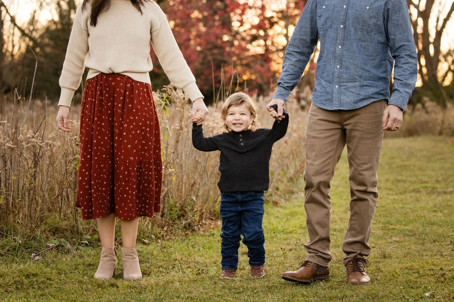 Child holding hands with two adults during sunset family pictures at Tinker Park