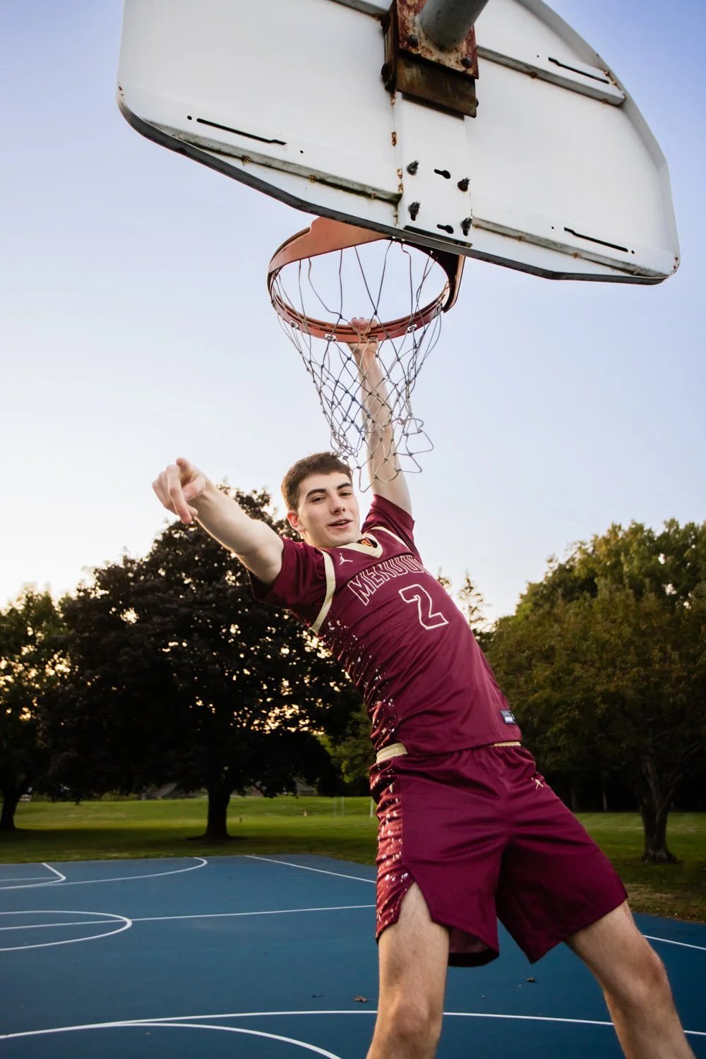 Pittsford Mendon NY senior photo session capturing athlete hanging from basketball hoop at sunset