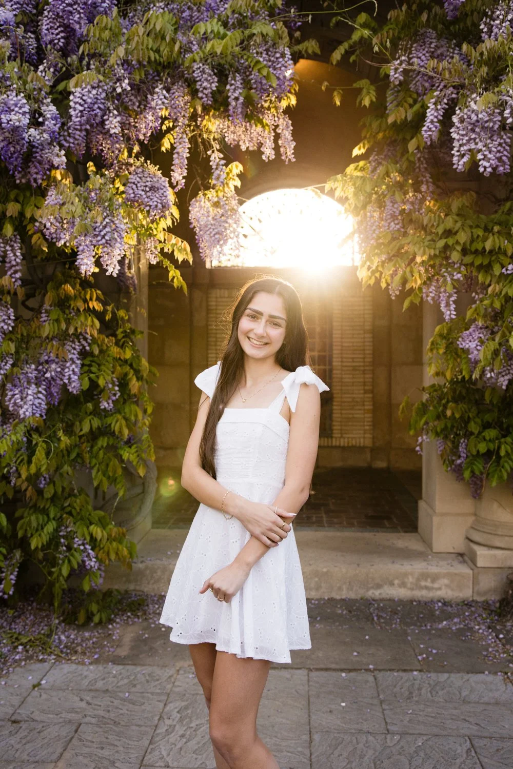 Eastman Museum senior photo session with senior in white dress beneath purple wisteria arbor