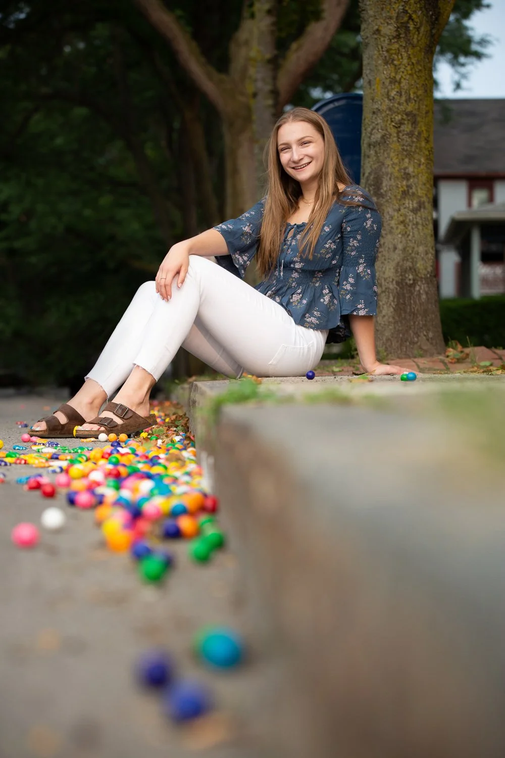 High school senior girl sitting on Park Avenue curb in Rochester NY surrounded by bright gumballs