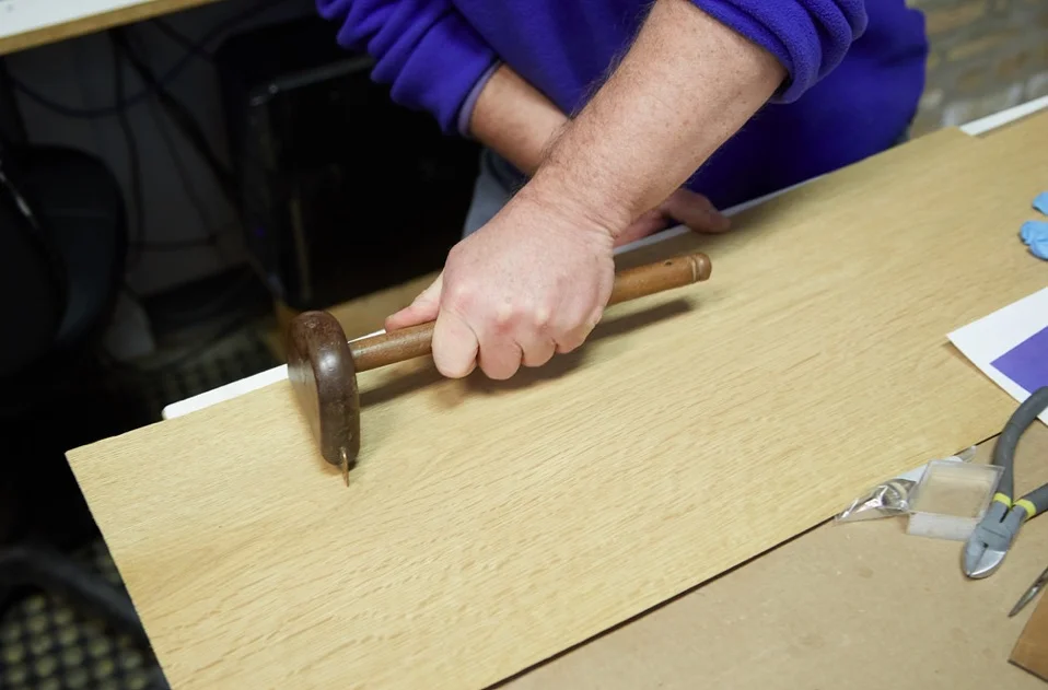 A veneer hammer acts like a squeegee and iron combo to level and hold veneer down as glue hardens. Used in place of a modern hydraulic clamp.