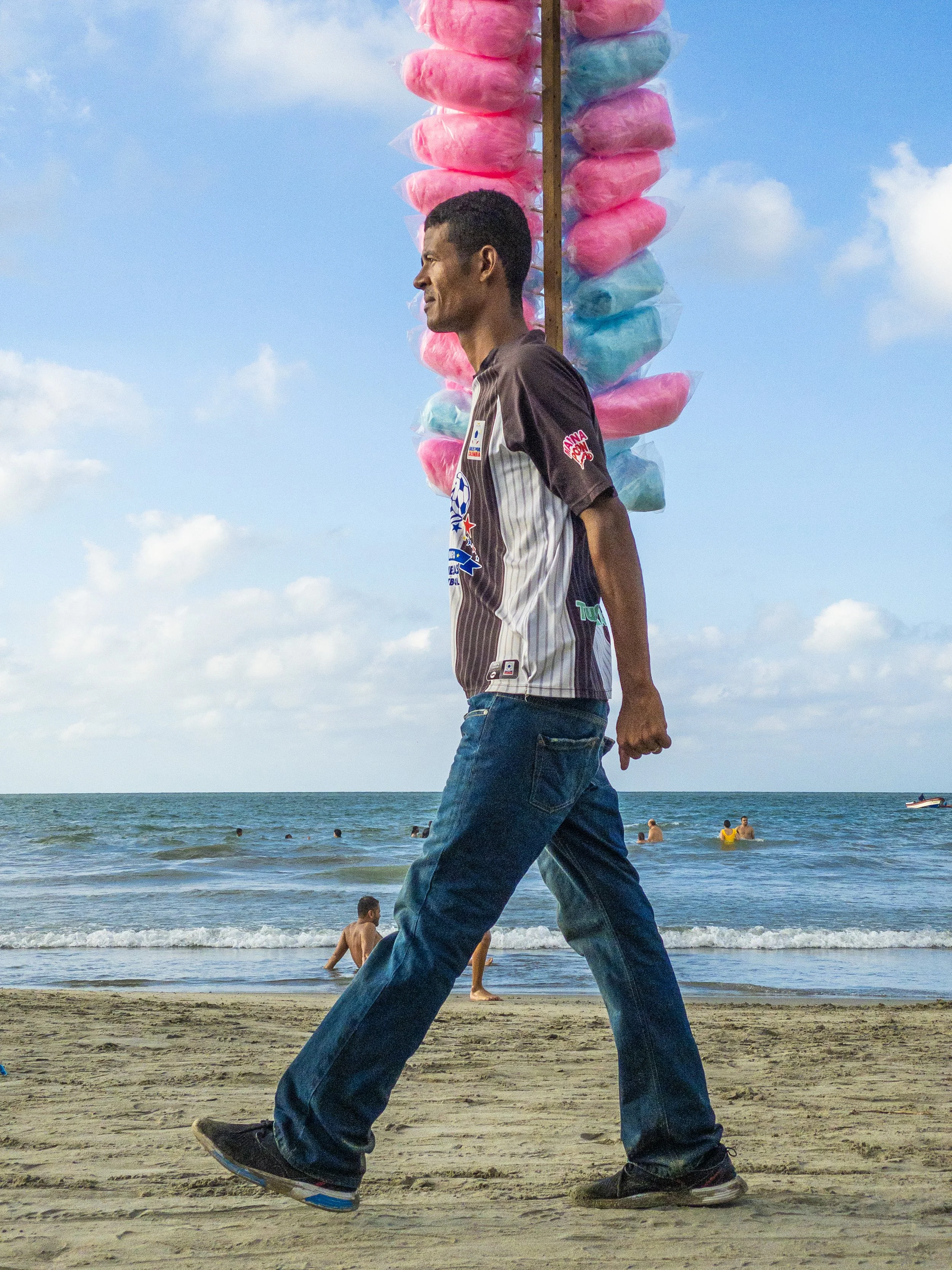 Beach trader carrying a pole of pink candy floss along the shore, from James Coulson's Beach Traders photography