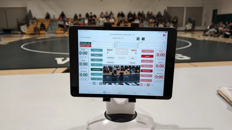 An iPad on a tabletop stand at the scorer's table, showing the Takedown scoring screen