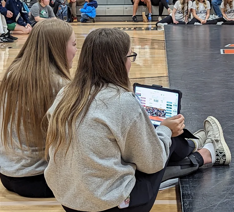Two student managers scoring a dual meet from the edge of the mat