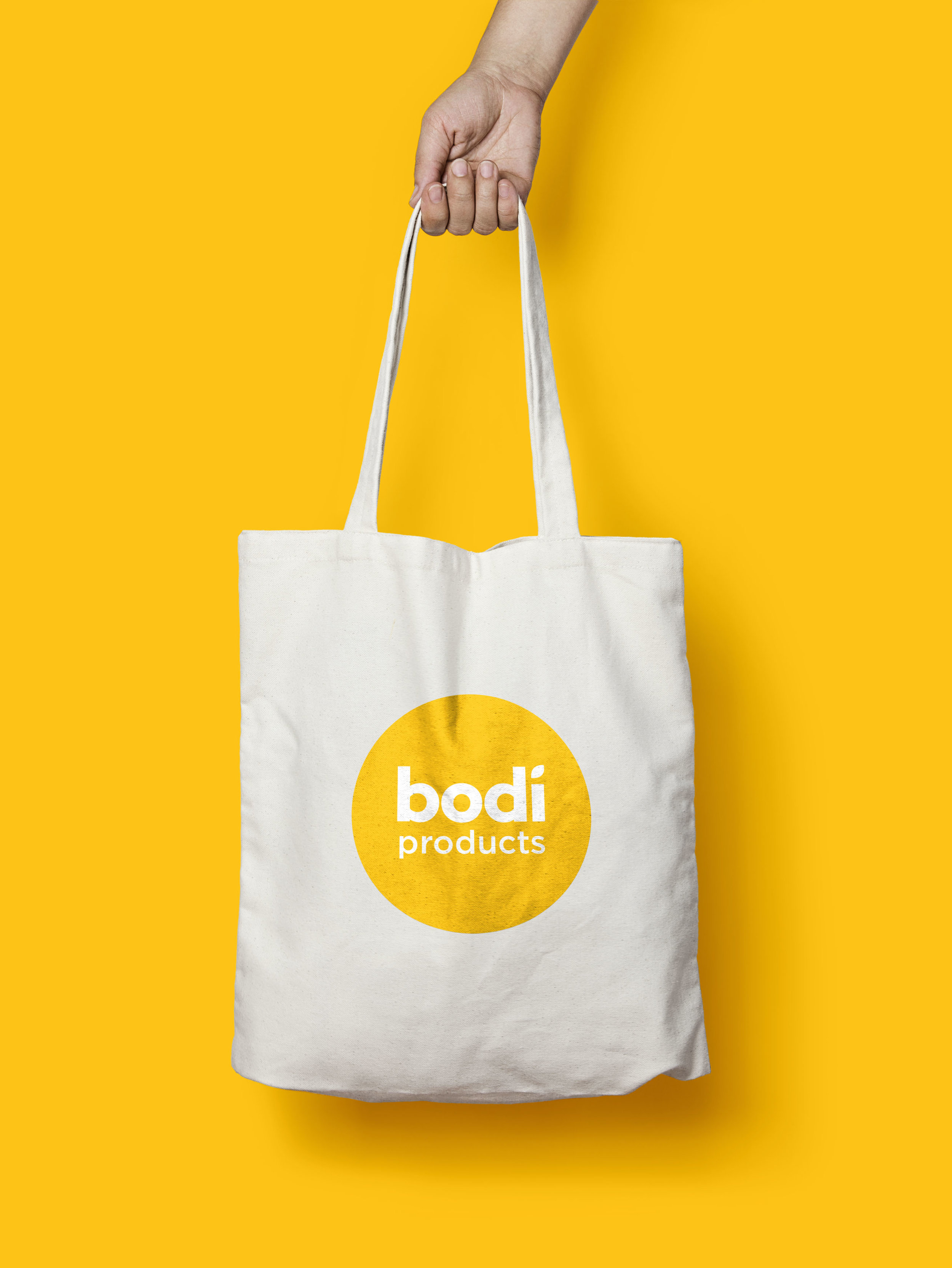 Packaging Designers UK A hand holding a Bodi branded white tote bag in mustard background