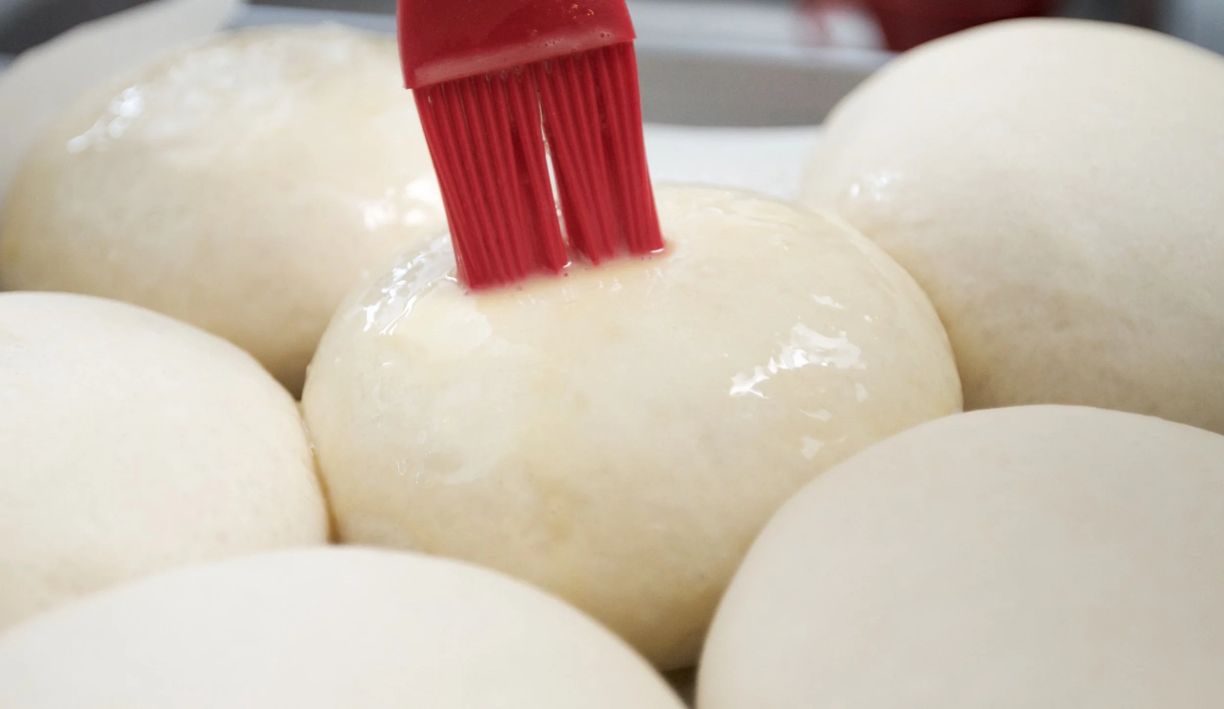 Brushing egg wash on the buns after they rise on the pan