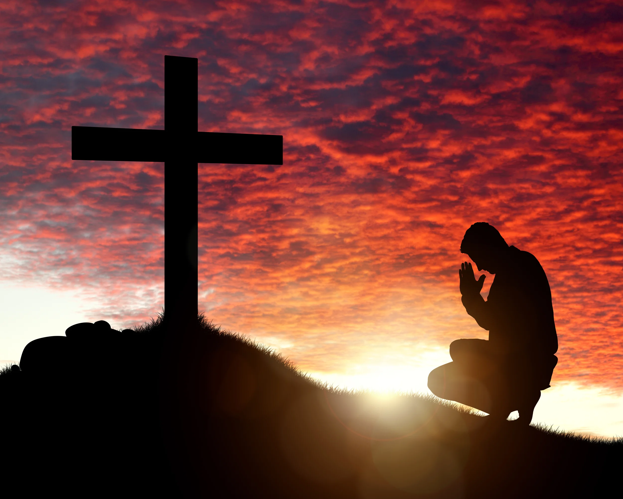 Silhouette of man praying to a cross with heavenly cloudscape su