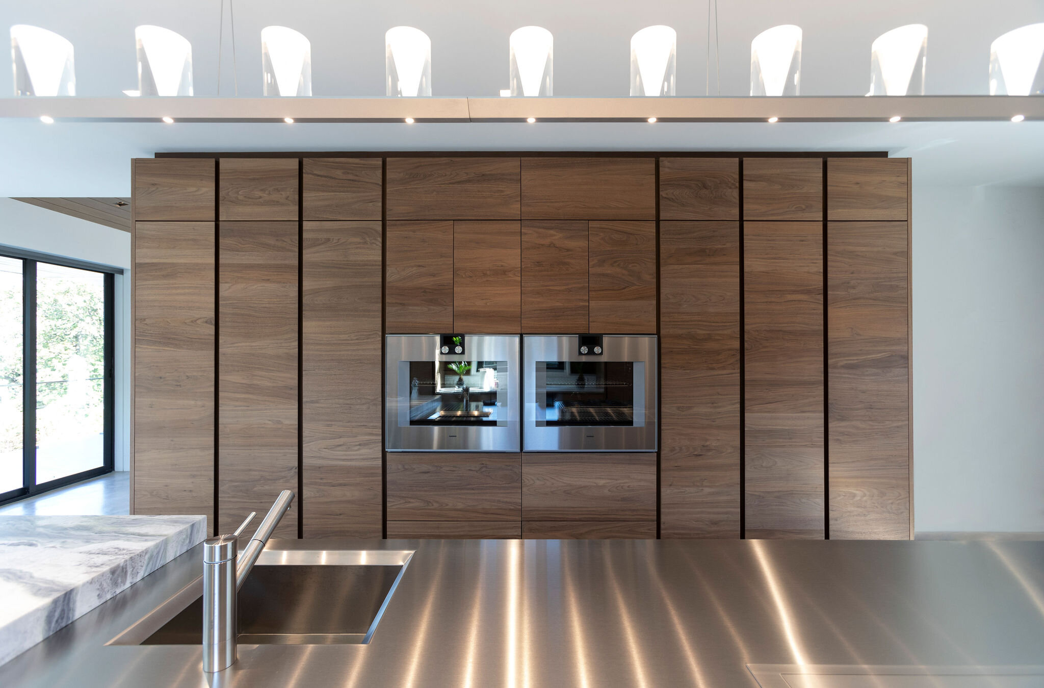  Wall ovens are flanked by hand-planed walnut cabinets that light up all interior shelves. The suspension lights over the island mimic candles when lit in the evening. 