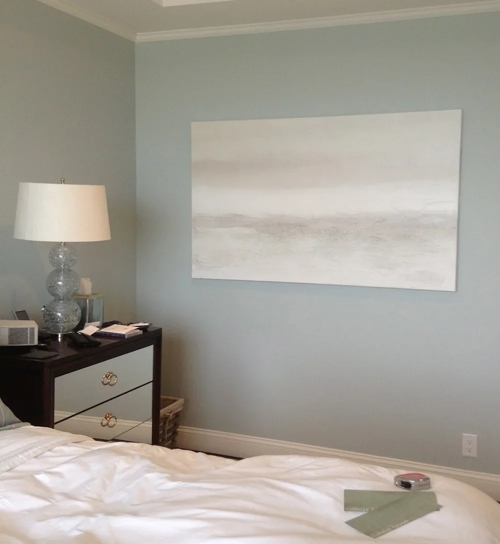 A bedroom with a bed, nightstand, lamp, and a large abstract painting on the wall.