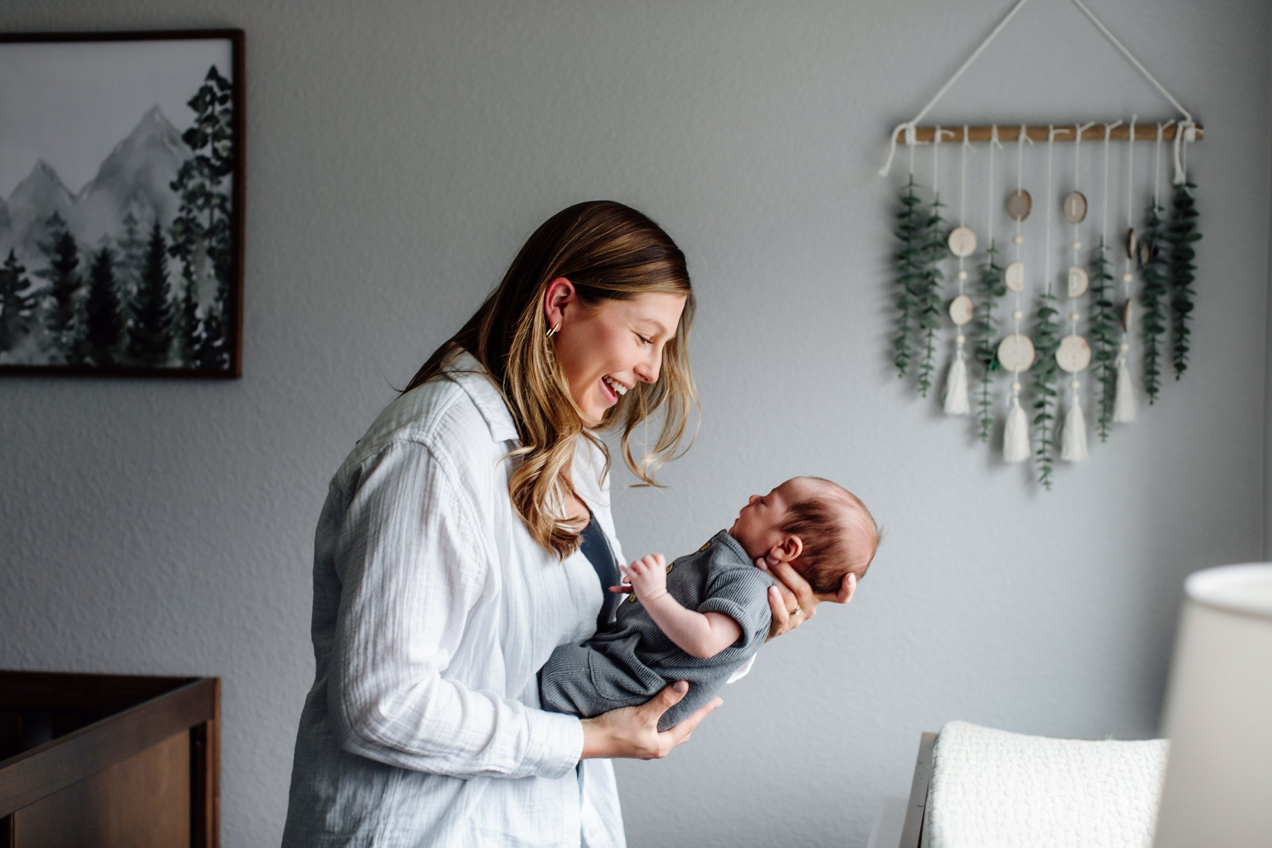 mom holding baby and looking at them fondly with smile denver newborn photo session lifestyle in home infant portraits