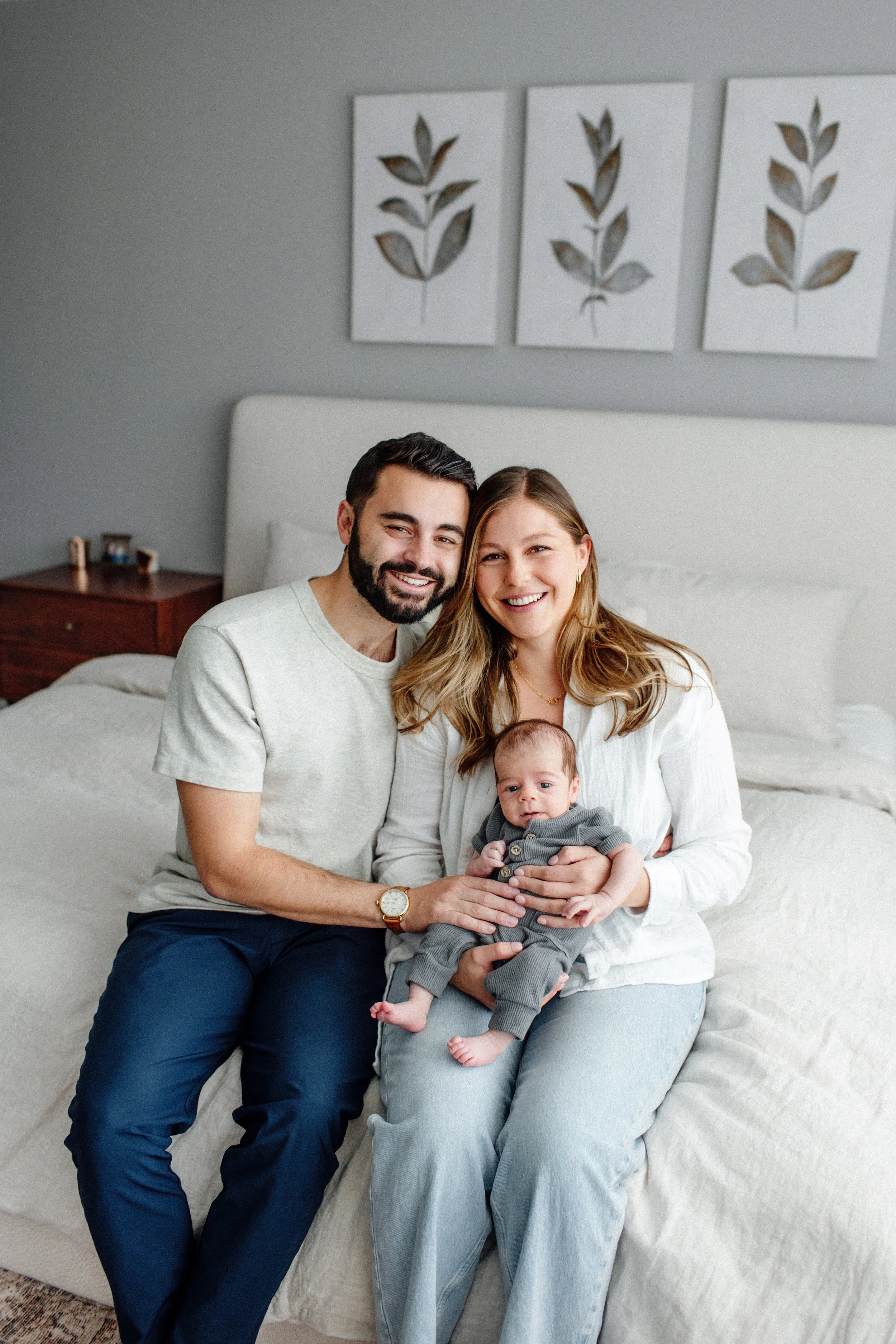 Parents sitting on bed holding newborn during in-home lifestyle newborn session in Denver, Denver Lifestyle newborn session in home with newborn infant