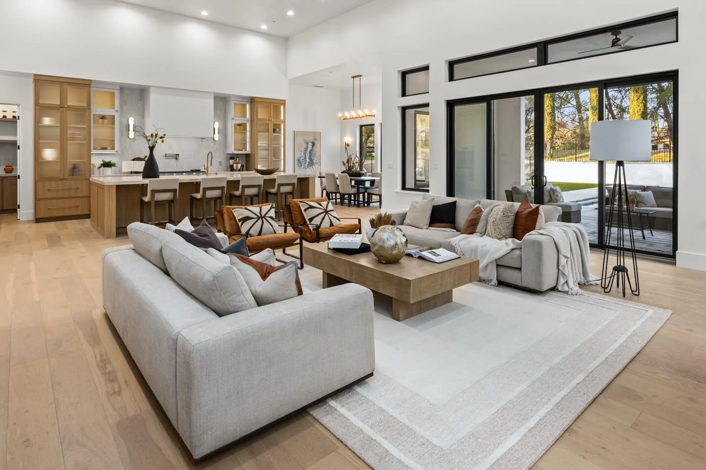 An exquisite open-concept great room showcasing a chef-inspired kitchen with bespoke wood cabinetry, a grand island, and designer lighting that flows seamlessly into a sophisticated, light-filled living area. Soaring ceilings and expansive glass crea
