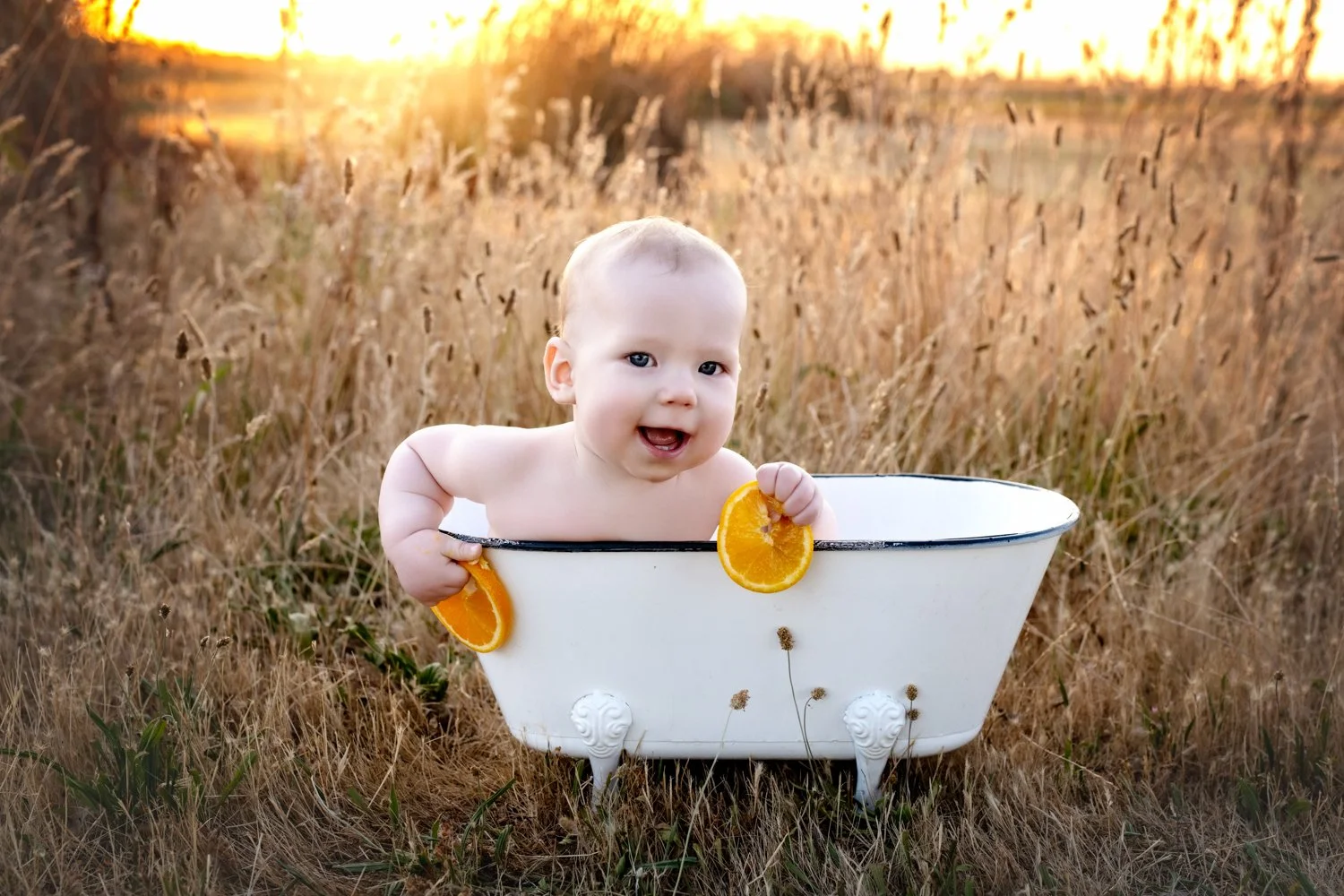 A six-month-old baby sitting in a bath tub splashing and smiling with a sunset during a milestone photography session in Lodi