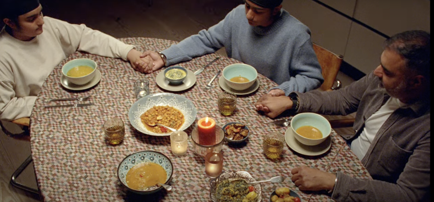 Family of three sitting around a dinner table. Screenshot from The Moment You Stand campaign.