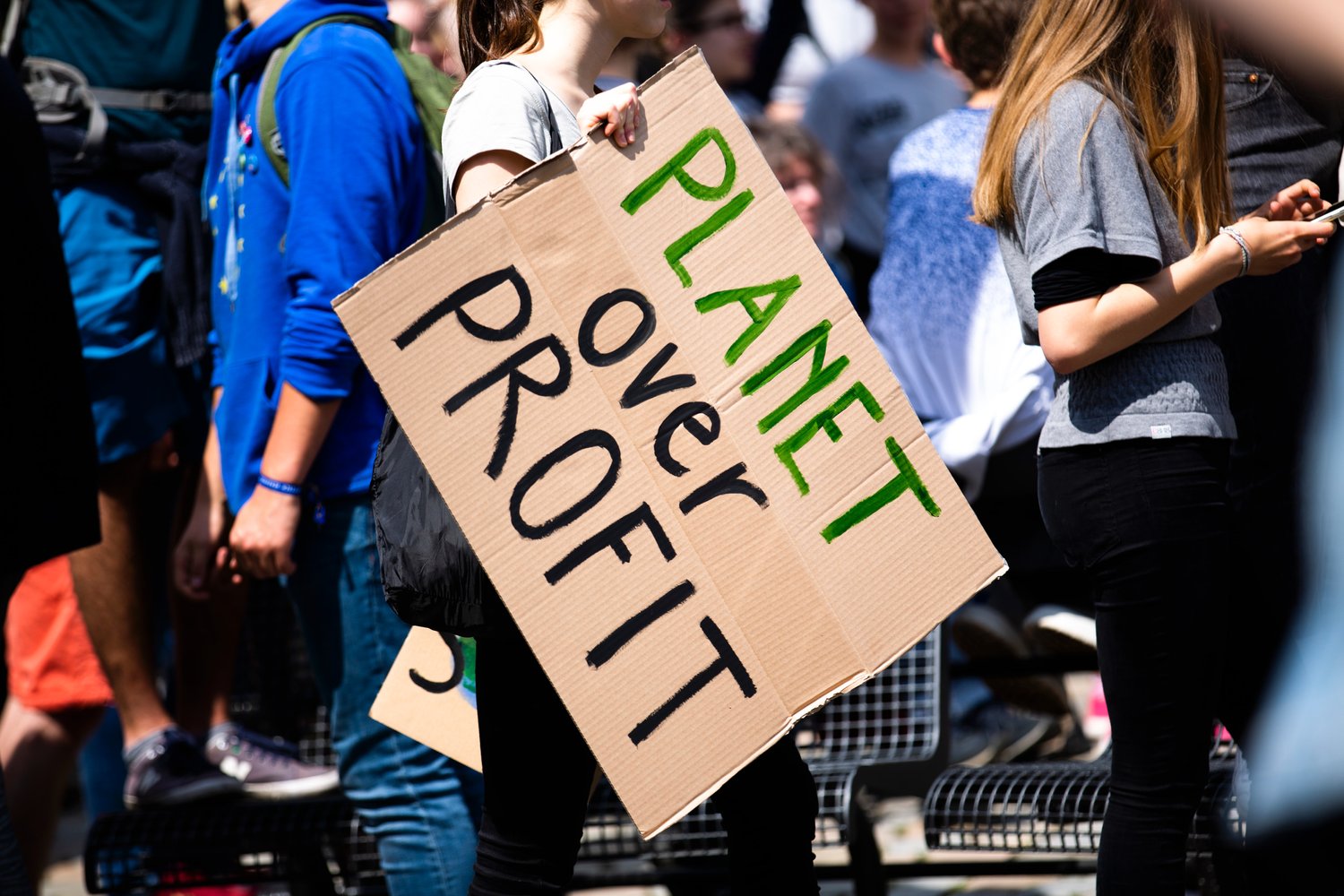young person at protest holding a sign saying 'planet over profit'