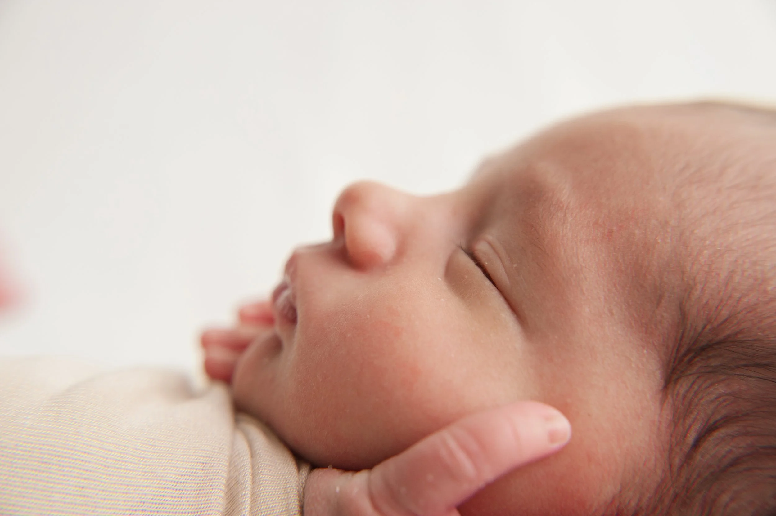 Close-up of a sleeping baby's face and hand, resting on a soft surface in Littleton Colorado.