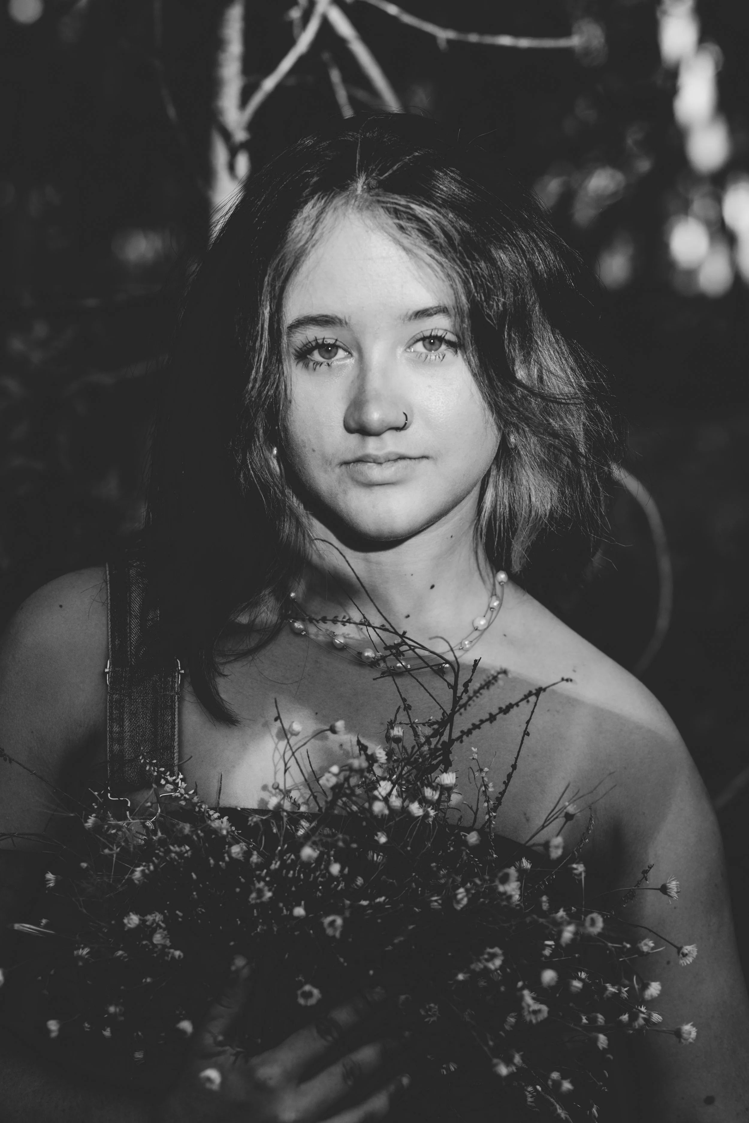A portrait of a young woman senior in high school with shoulder-length hair holding a bouquet of wildflowers, looking at the camera, outdoors in natural lighting, black and white photograph Cherry Creek Reservoir