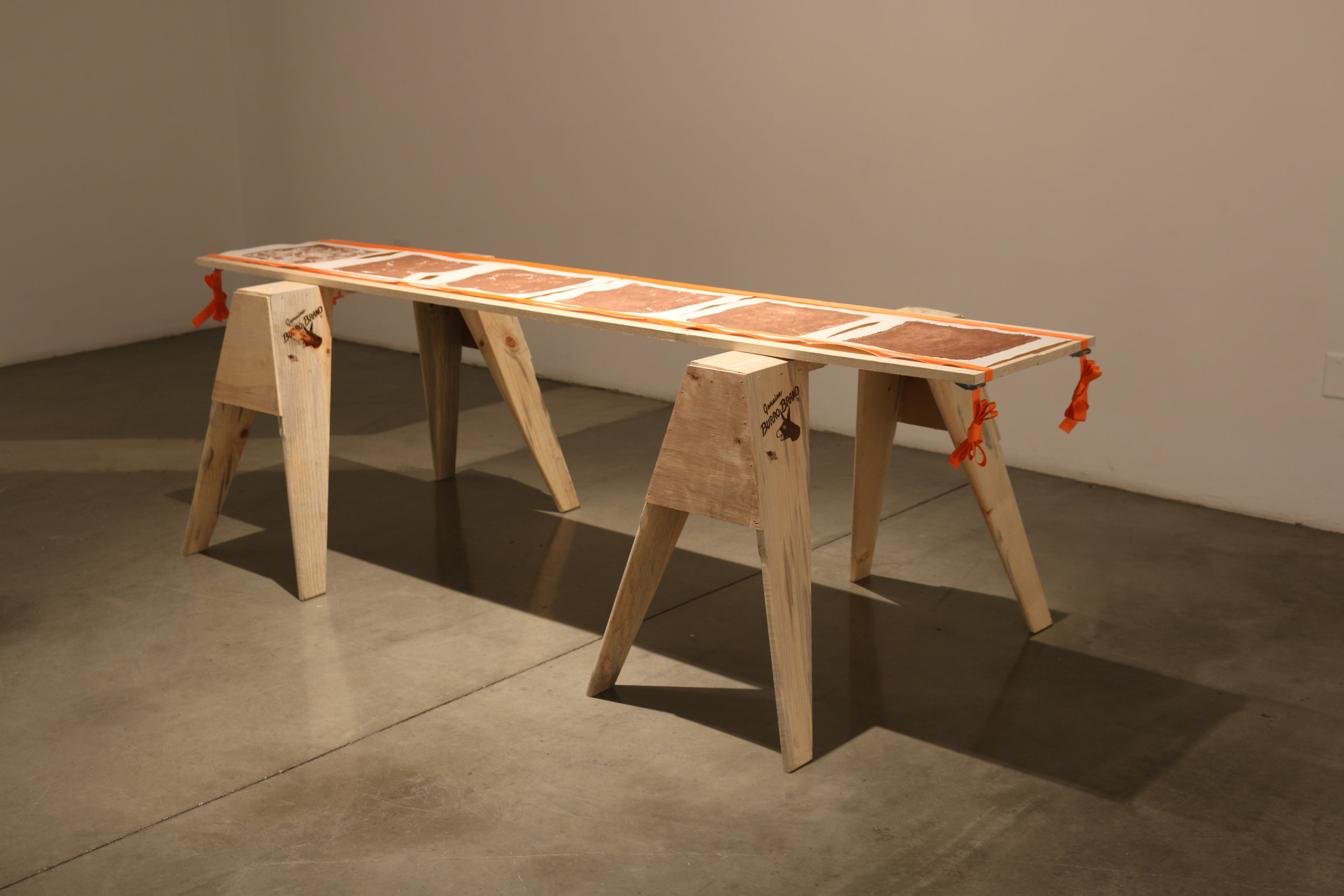   la mancha , 2018   sawhorses, common board, orange furniture straps, terracotta clay, arches archive paper. 24” x 3’ x 8’   