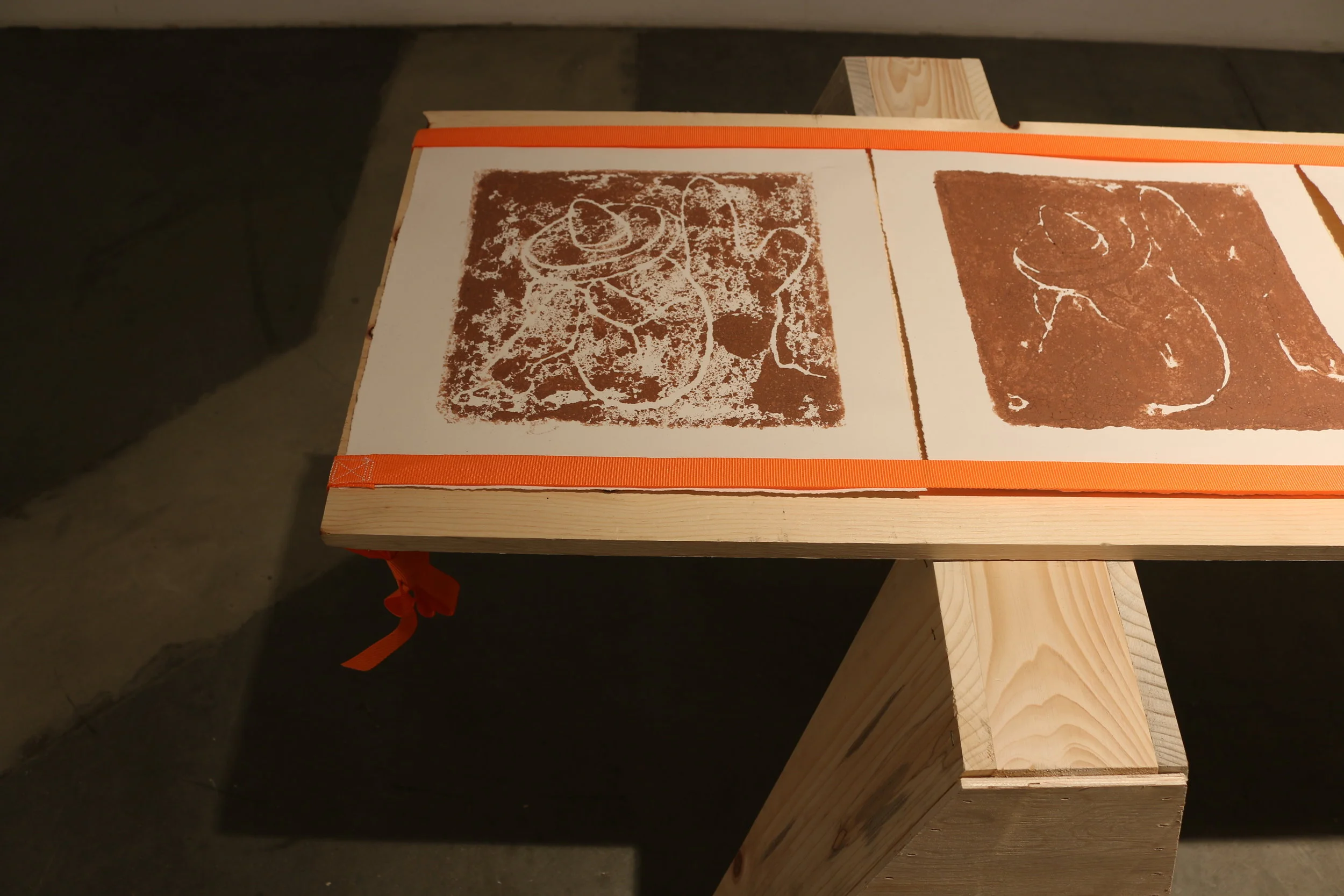   la mancha , 2018   sawhorses, common board, orange furniture straps, terracotta clay, arches archive paper. 24” x 3’ x 8’ 