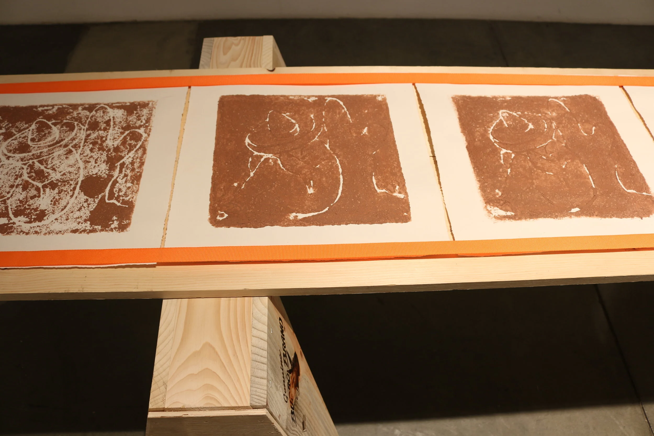   la mancha , 2018   sawhorses, common board, orange furniture straps, terracotta clay, arches archive paper. 24” x 3’ x 8’ 