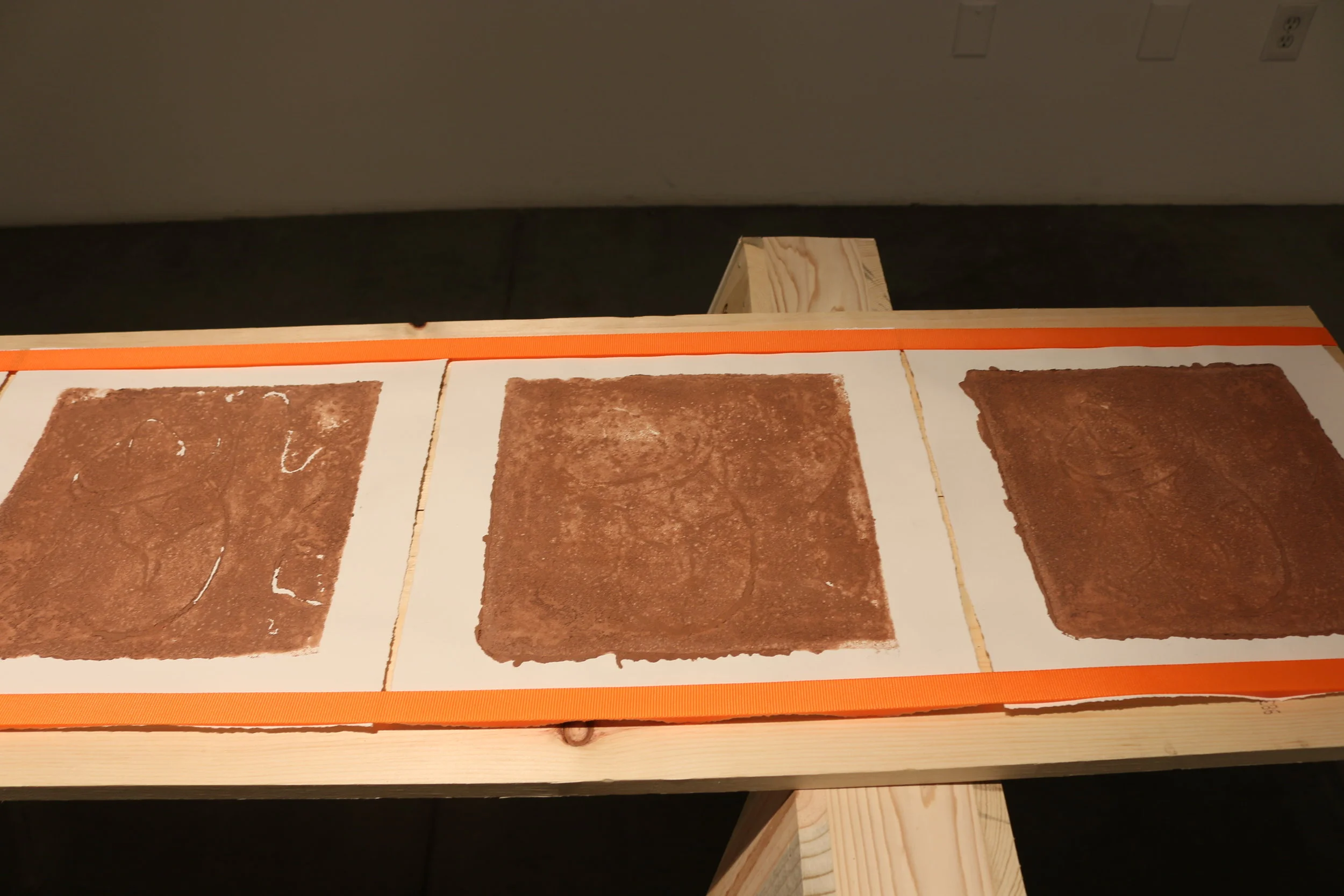   la mancha , 2018   sawhorses, common board, orange furniture straps, terracotta clay, arches archive paper. 24” x 3’ x 8’ 