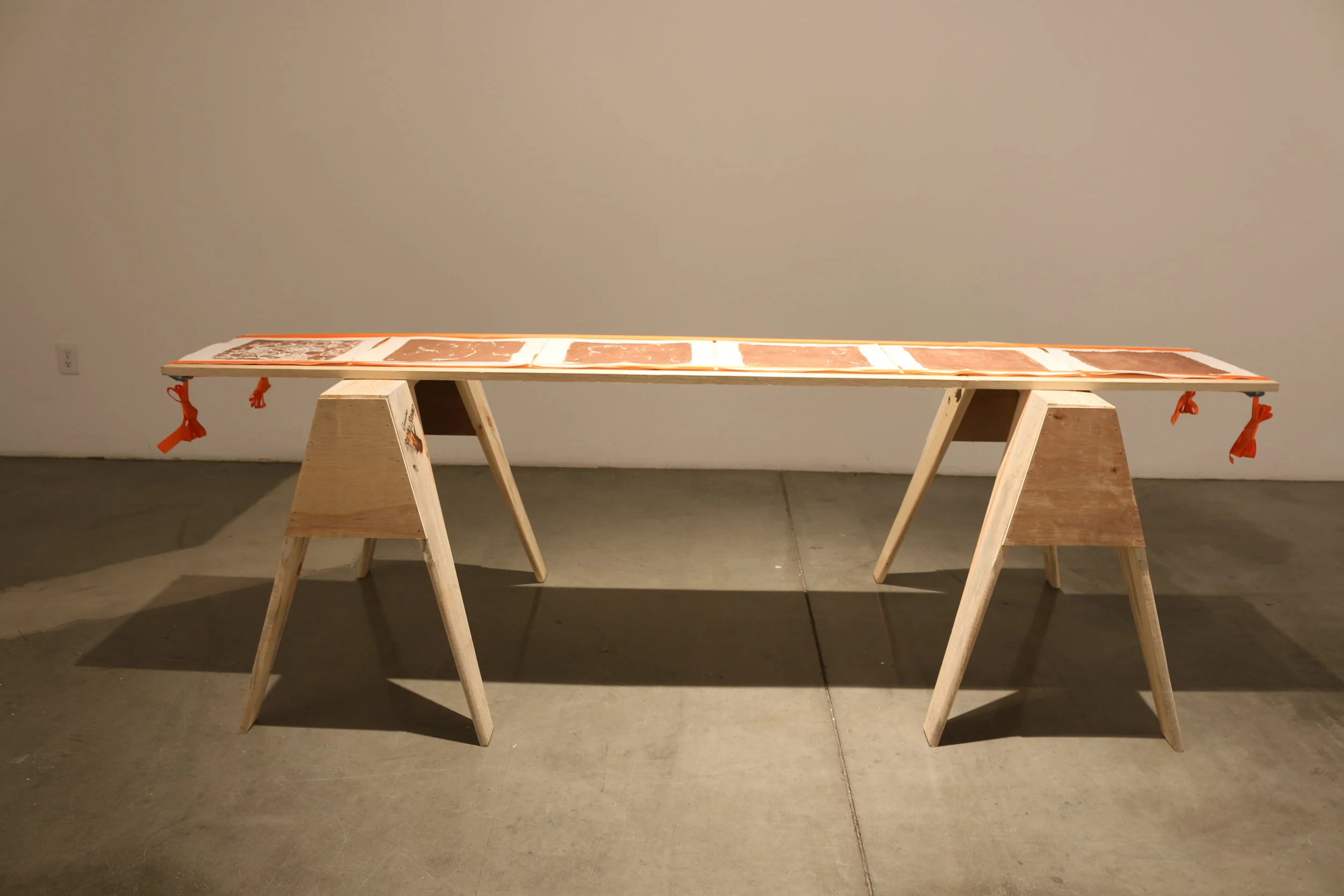   la mancha , 2018   sawhorses, common board, orange furniture straps, terracotta clay, arches archive paper. 24” x 3’ x 8’ 