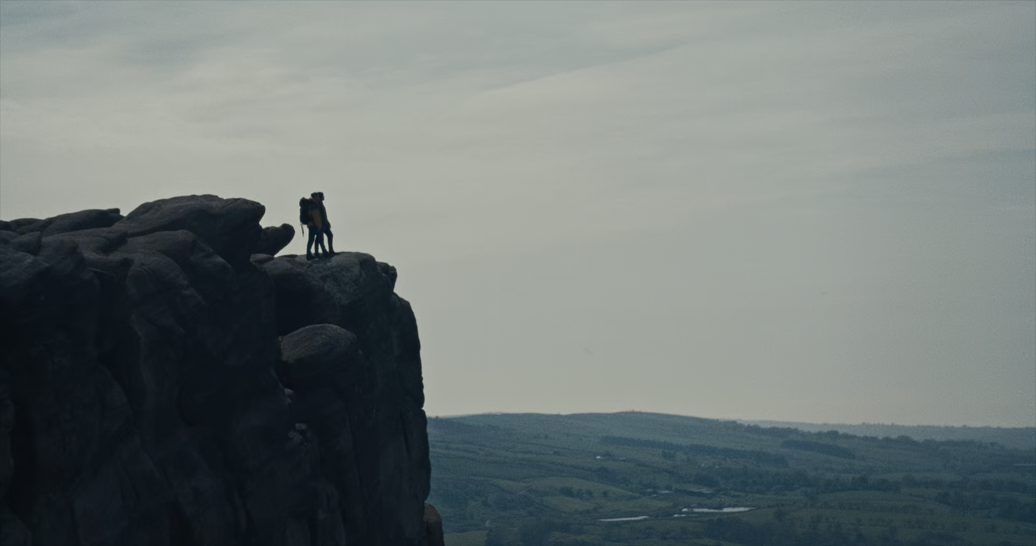 Two men stand side-by-side at the edge of a cliff, looking out towards the distant horizon.
