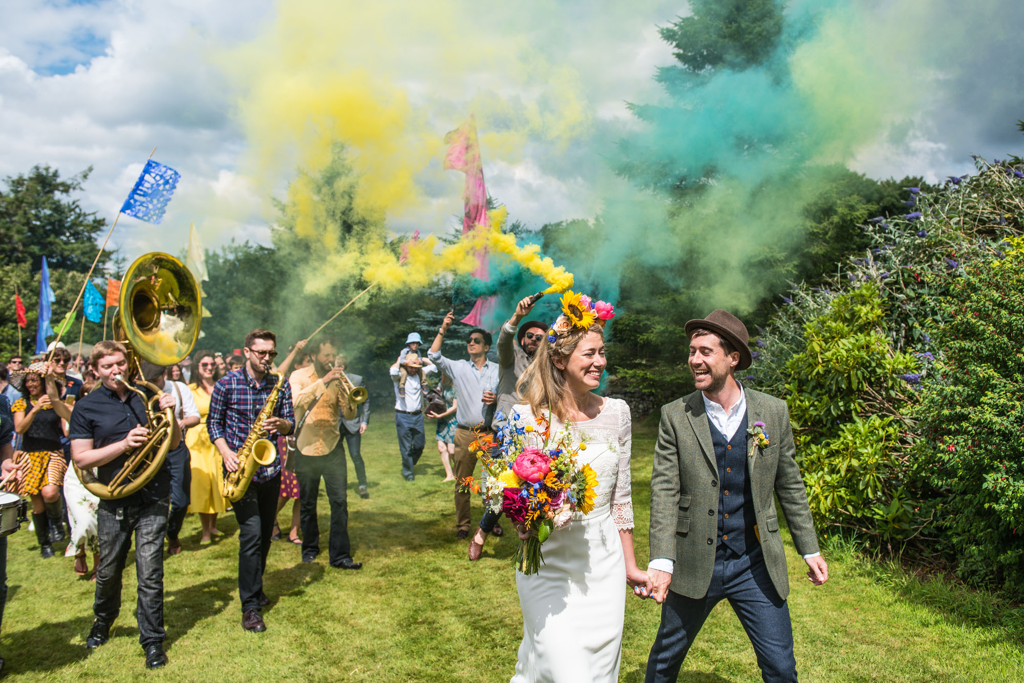 Colourful smoke bombs and brass band follow bride and groom during festival themed wedding in Devon