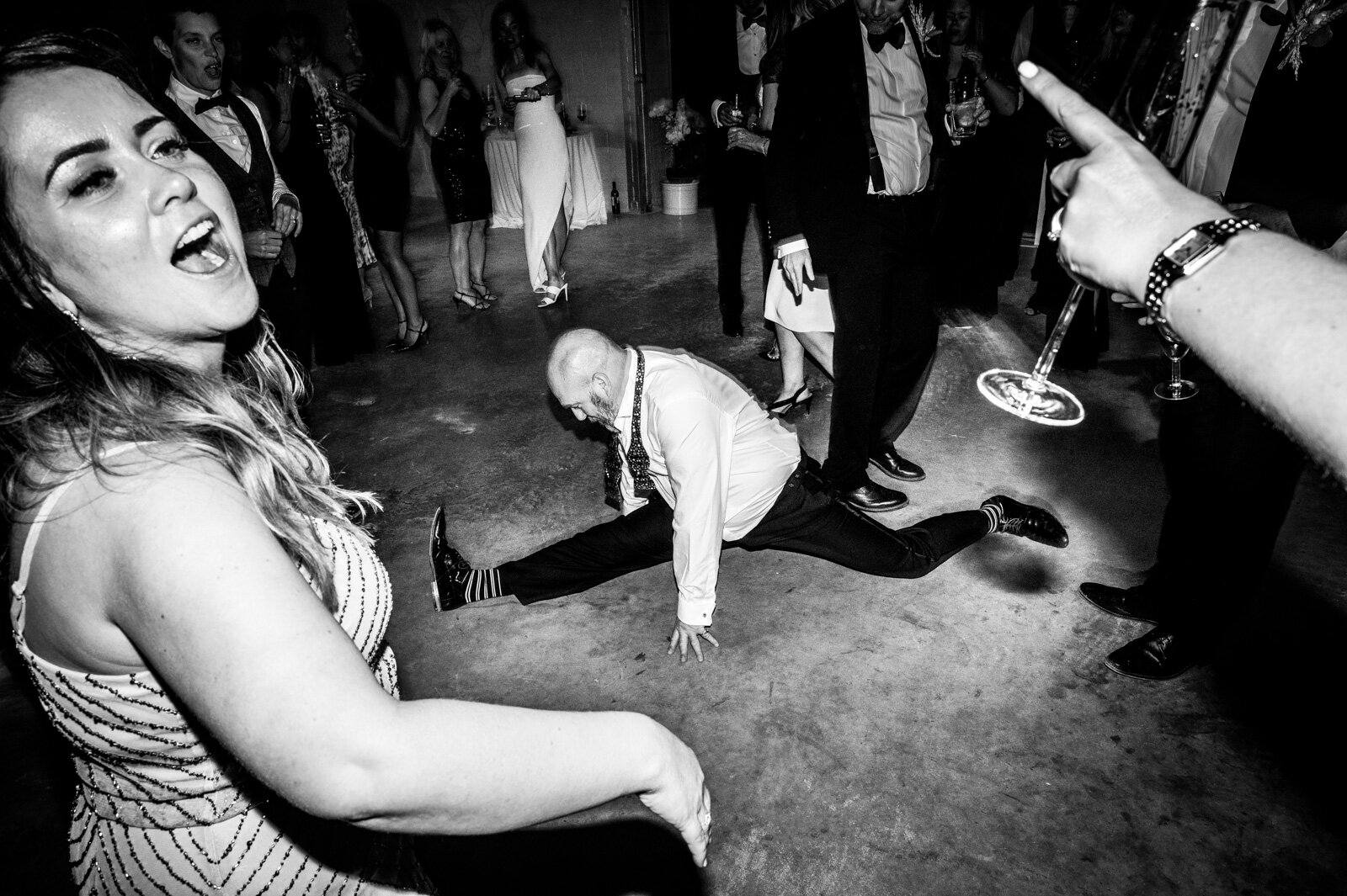 black and white image of male wedding guest doing the splits on dance floor