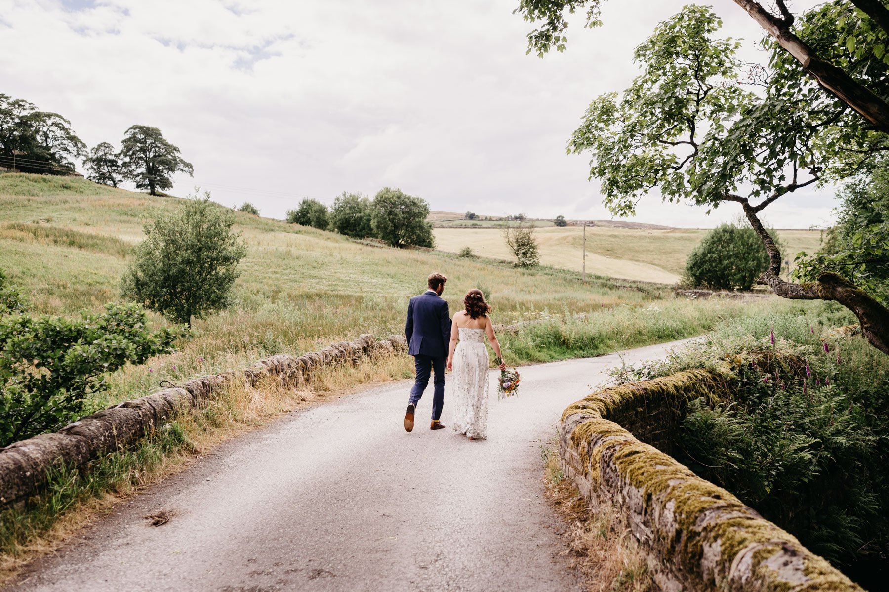 wedding portrait of bride and groom walking over bridge with views of Yorkshire dales